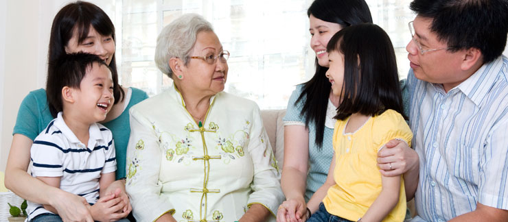 Happy elderly female woman sits on couch with her three grandchildren and their parents.