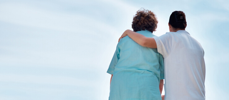 Female home care aide puts arm around senior woman as they both look up to the sky outside.