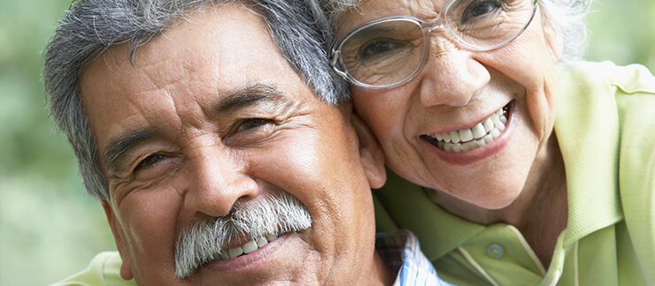 Senior couple smiles while embracing each other outside.