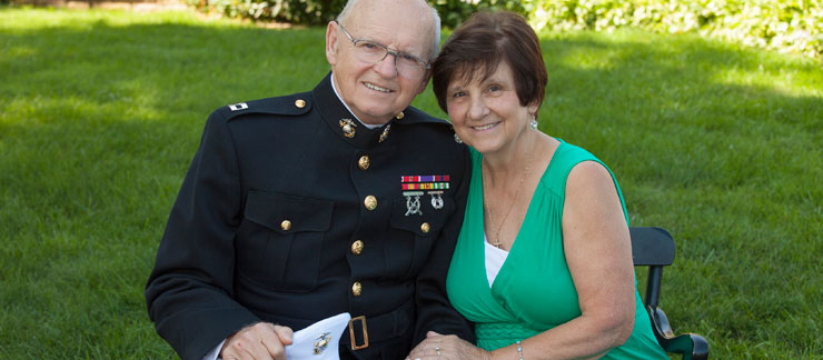 A smiling male veteran dressed in a military uniform sitting with wife on a park bench.