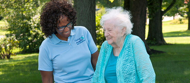 Female caregiver assists elderly woman during walk in the park.