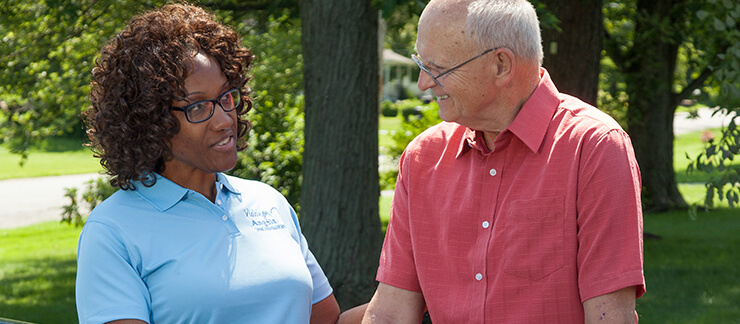 Female care worker converses with senior man on a walk through park.