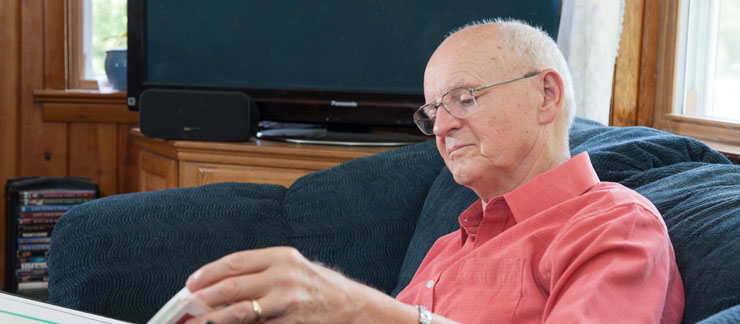 Senior male sits on a sofa while reading a book.
