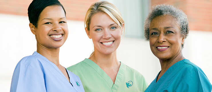 Three female professional home caregivers smiling outside.