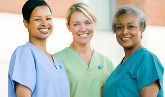 Three female professional home caregivers smiling outside.