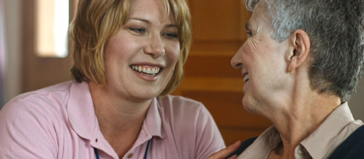 Female care provider and senior woman share a laugh at home.