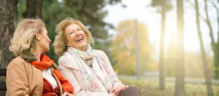 Two senior woman laugh while sitting on a park bench during a brisk afternoon.