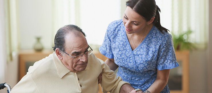 Senior male in wheelchair gets assisted by female care worker.