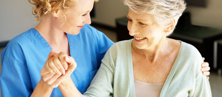 Female home care worker grips the hand of a smiling senior woman.