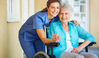 Female care provider holds hand of senior woman sitting outside in a wheelchair.