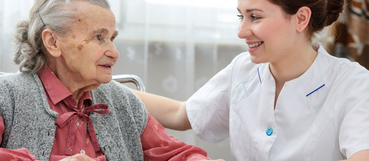 Elderly woman sitting on chair smiles at female home care aide.