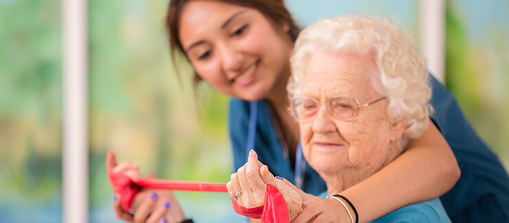 Care aide helps elderly woman with hand strength exercises.