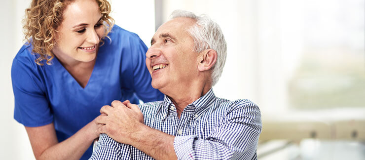 Home care worker rests hand on happy senior man sitting at home.