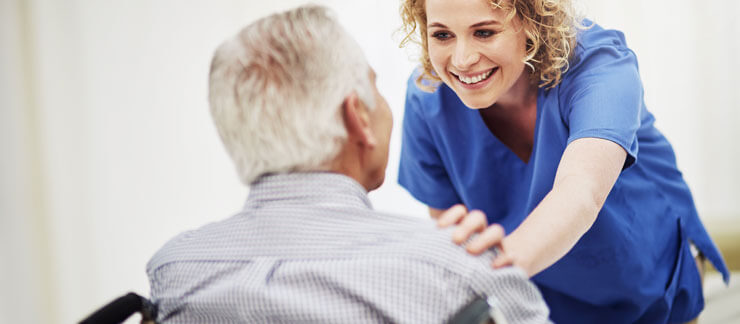 Female care provider comforts senior male in wheelchair.