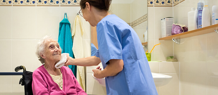 Elderly woman in bathroom gets her face washed from helpful home care worker.