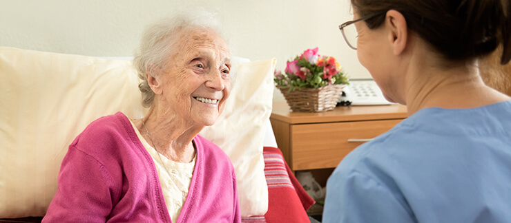 Elderly woman in bed smiles at an attending home care aide.
