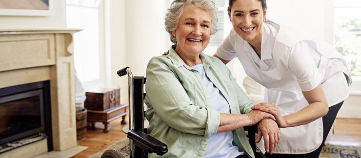 Senior care provider places hand on a senior woman's hand sitting in a wheelchair at home.