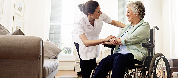 Female care worker places hand on elderly woman in a wheelchair who just returned home from surgery.