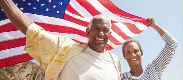 Happy couple proudly hold American flag over their heads outside.