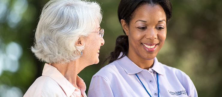 Senior woman smiles while talking to a female Visiting Angels care provider outside.