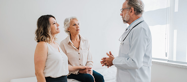 Senior parent and adult daughter speak with a doctor in his office.