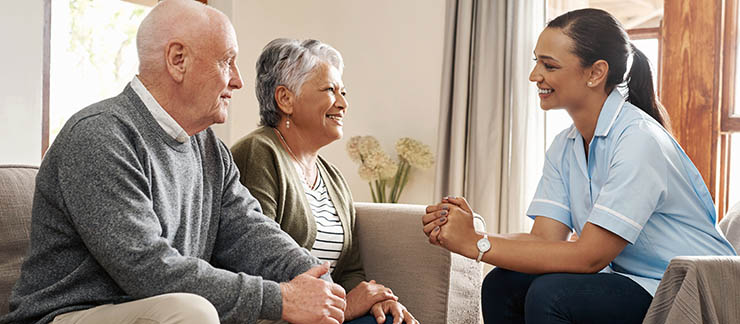Female care coordinator discusses home care services with senior couple at home.