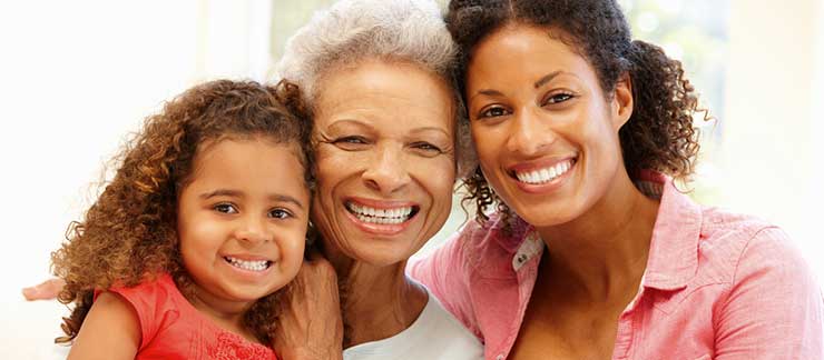 Senior female smiles with daughter and young granddaughter.