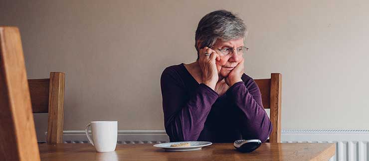 Elderly woman sits alone at breakfast table waiting for telephone to ring.