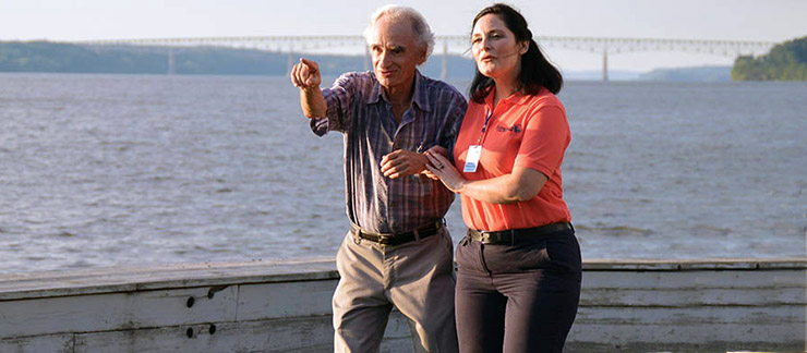 Elderly man showing early signs of dementia takes a walk with female caregiver near the river.