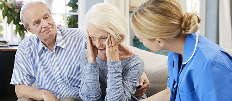 Woman suffering from dementia is comforted by husband and in-home caregiver.