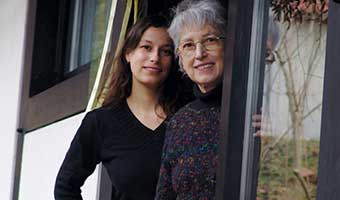 Senior woman smiling with female caregiver at the front door.