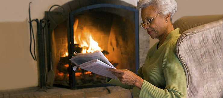 Senior reading near fireplace.