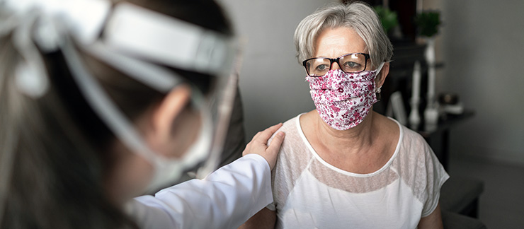 Senior with mask is comforted at home by caregiver during flu season and COVID-19 pandemic.