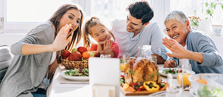 Senior woman and her family during a holiday meal saying hello to loved ones virtually through computer.