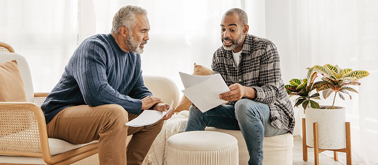 Senior man and his adult son sitting at home looking at home care insurance papers.