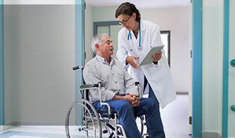 Senior man in wheelchair getting discharge directions at the hospital from a female physician.