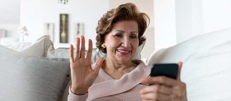 Senior woman waves hello to family during a video chat on her phone.