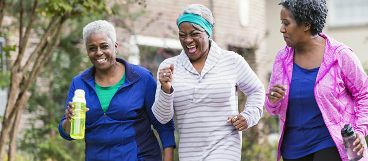 Three senior African-America women exercising together by power walking along a sidewalk in a residential neighborhood. They are having fun, laughing.