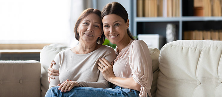Senior woman and adult daughter sitting on couch smiling together at home.