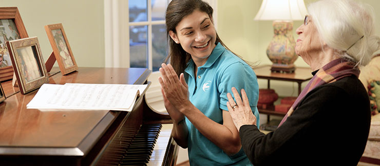 Female care worker applauds after elderly woman finishes playing the piano at home.