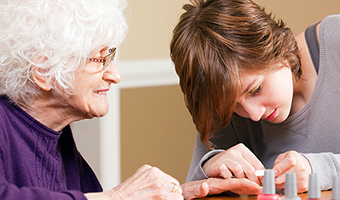 Female caregiver grooms senior woman's nails at her home.