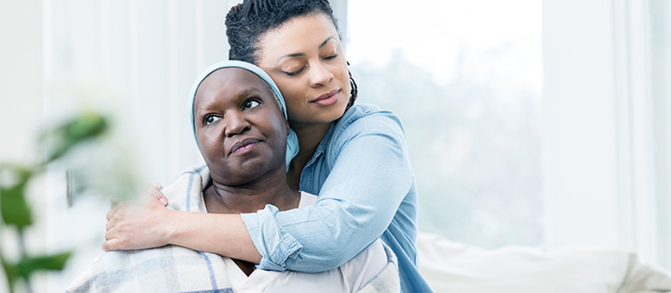 Daughter hugs senior parent who is managing a chronic illness at home.