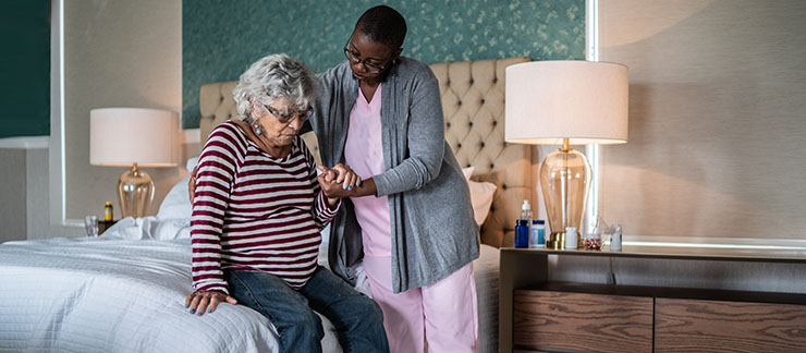Female caregiver helps a senior with Parkinson's disease out of bed at home.