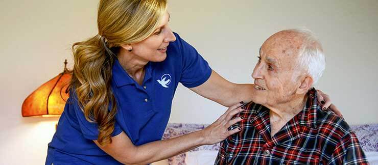 Female home care worker assists elderly man in home after returning from hospital.