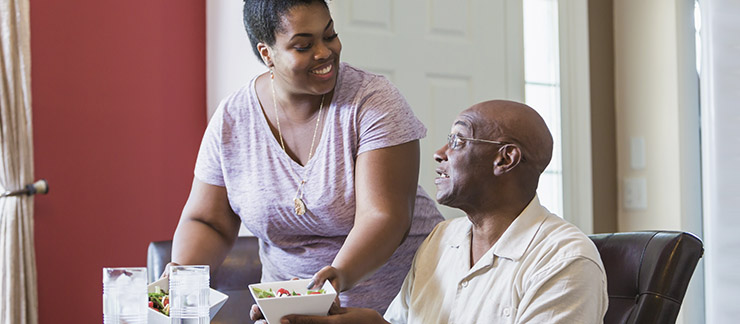 Female caregiver serves meal to elderly male at home as part of respite care services.