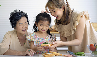 Asian grandmother, mother, and granddaughter happily prepare food in the kitchen.