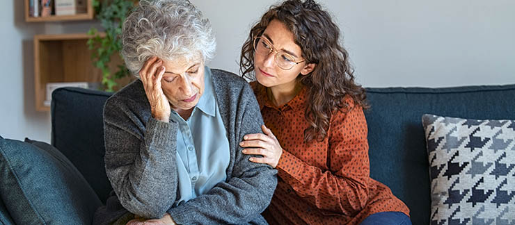 Caring young female comforting depressed senior woman on sofa at home.