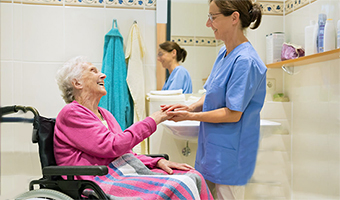 Female caregiver helps an elderly woman in a wheelchair to safely use the bathroom at home.