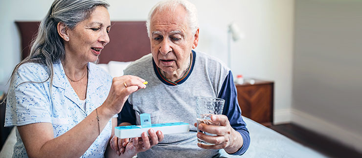 Female helps elderly man take medication using a weekly pill organizer.