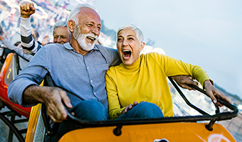 Senior couple having fun while riding on a rollercoaster at an amusement park.